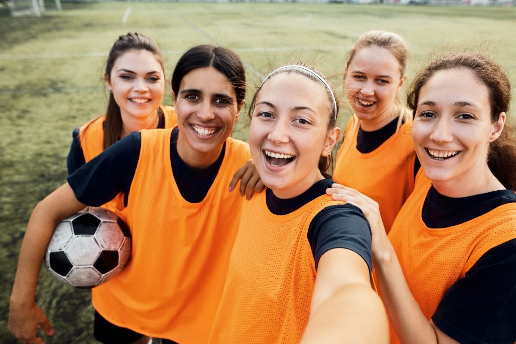 Cheerful women's soccer team taking selfie at the stadium.