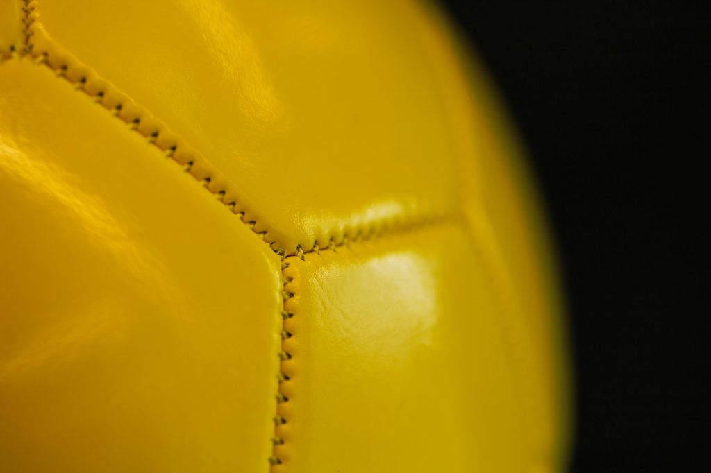 Close-up of the seams of a yellow sports ball on a dark background